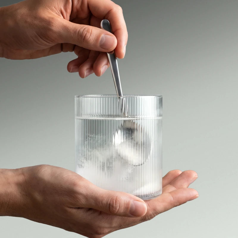 Imagen de unas manos diluyendo la creatina en un vaso de agua.